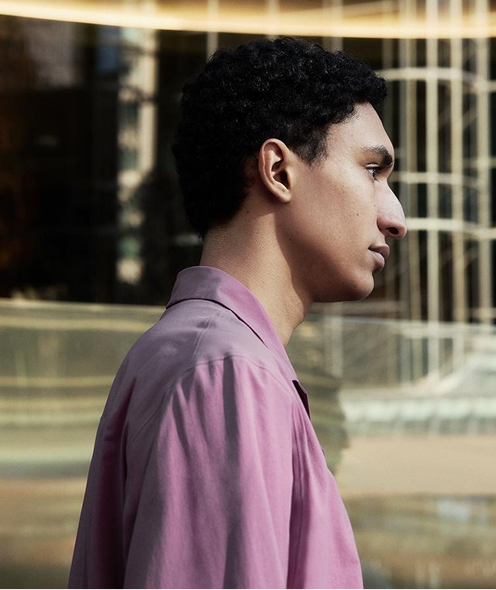 Profile of a person with dark, curly hair wearing a purple shirt, looking right.