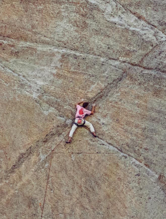 A person in a pink shirt rock climbing a large, textured rock face.