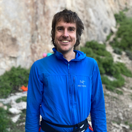 a man wearing a blue arcteryx jacket smiles for the camera
