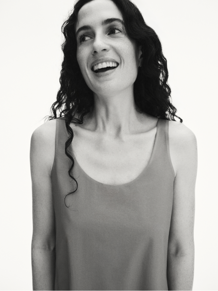 Black and white portrait of a joyful woman with long, dark curly hair smiling broadly and looking to the left.
