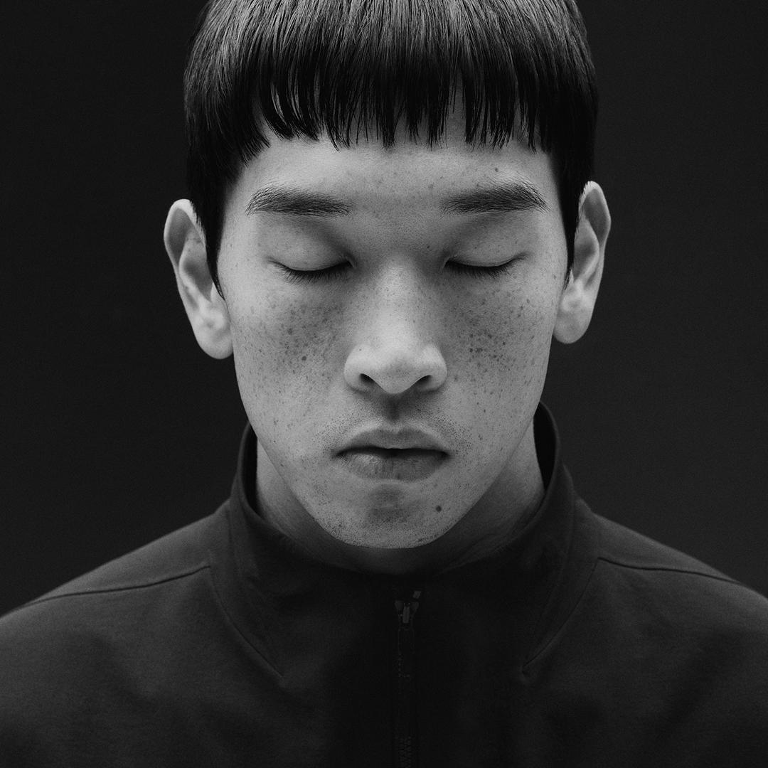 Black and white portrait of a person with closed eyes, short bangs, and freckles.