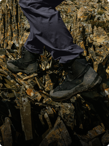 A person's legs in dark pants and hiking boots stepping on sharp, jagged rocks.