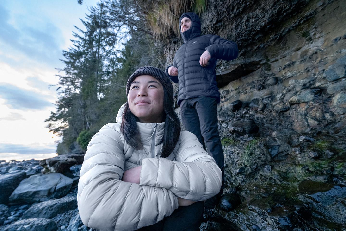 a man and a woman are standing next to each other on a rocky cliff wearing insulated down jackets
