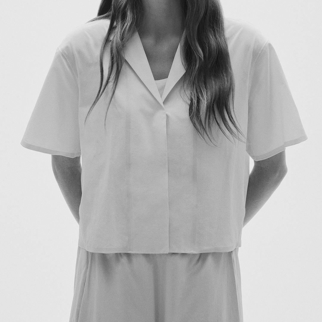 Monochrome image of a person wearing a white, short-sleeved top with an open collar.