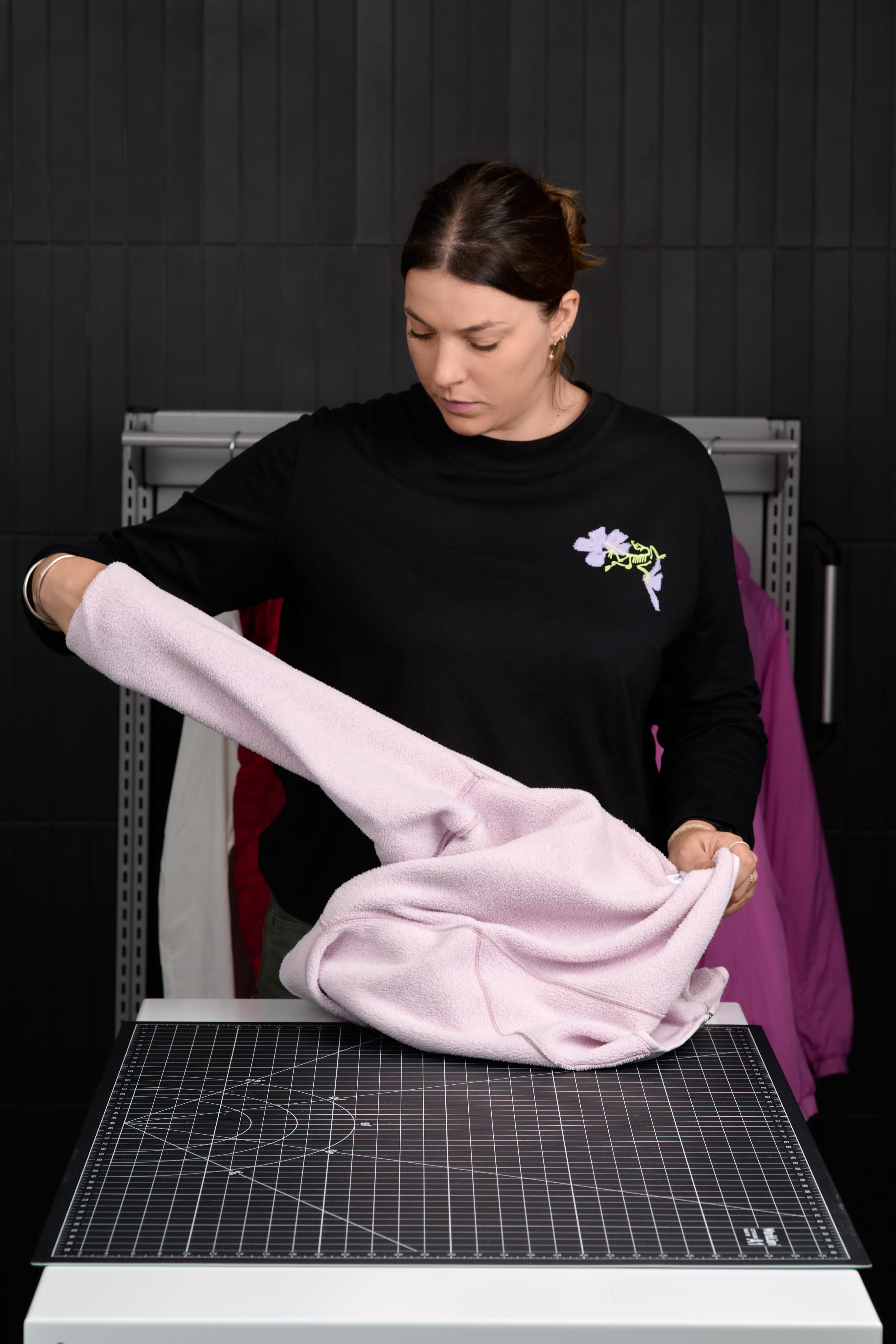 A woman in a black long-sleeved shirt folds a light pink garment on a table with a grid mat.