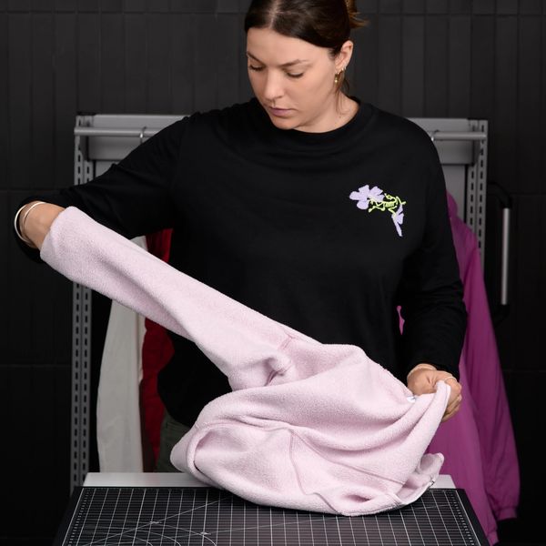 A woman in a black long-sleeved shirt folds a light pink garment on a table with a grid mat.