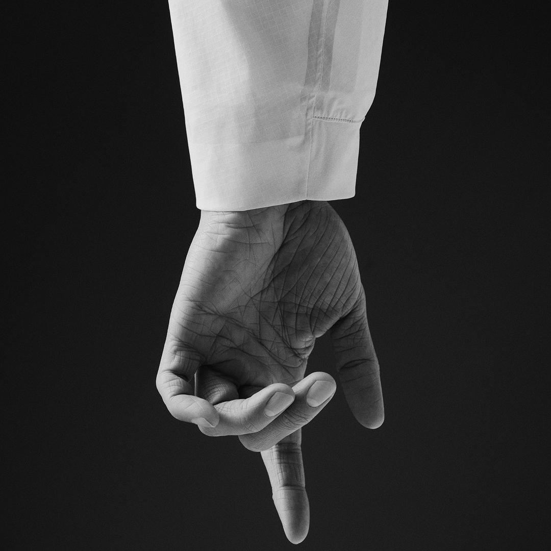 Black and white image of a hand in a white cuff, palm visible, with the index finger pointing down.