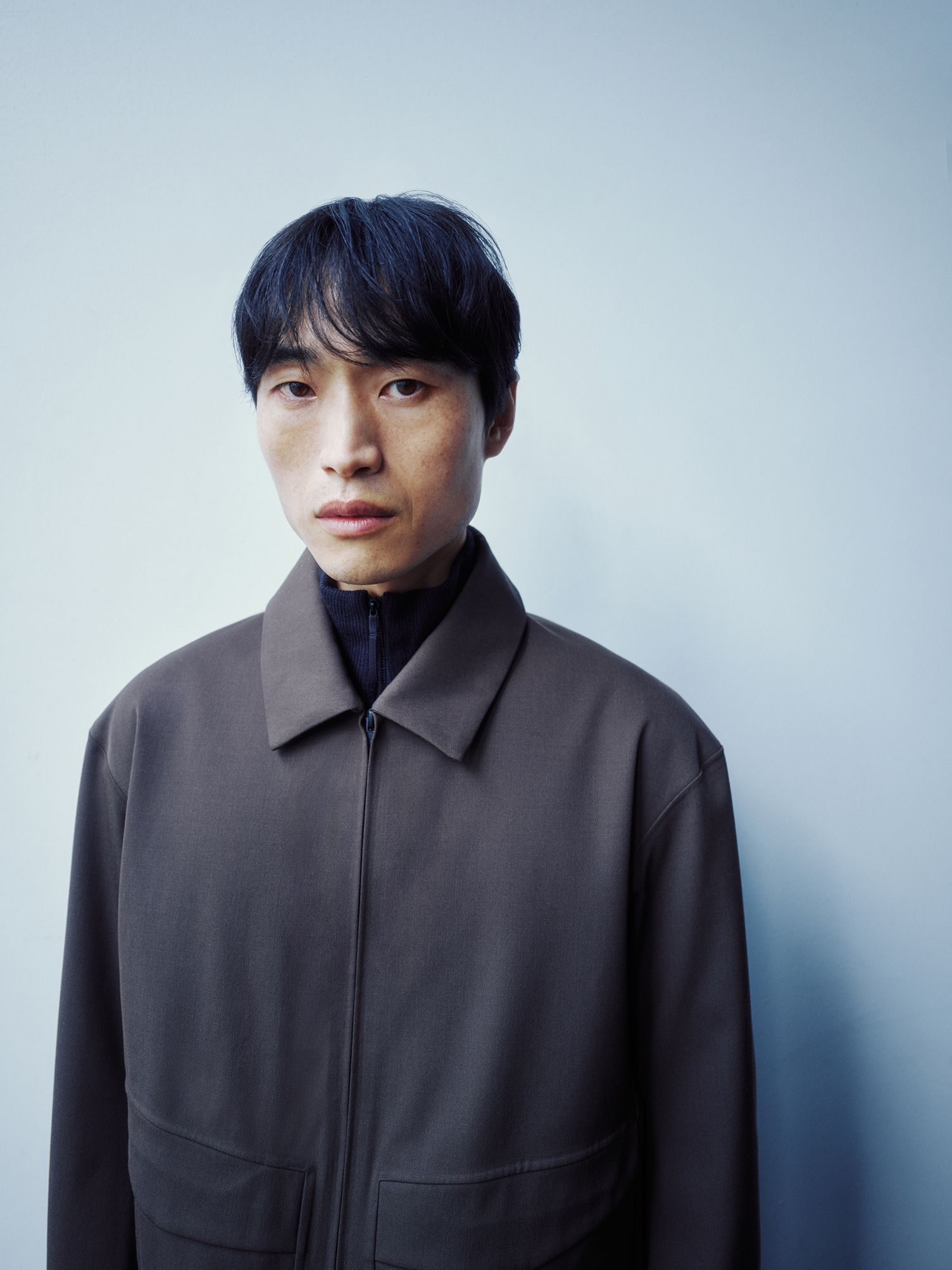 A man in a dark jacket and black turtleneck looks directly at the camera.