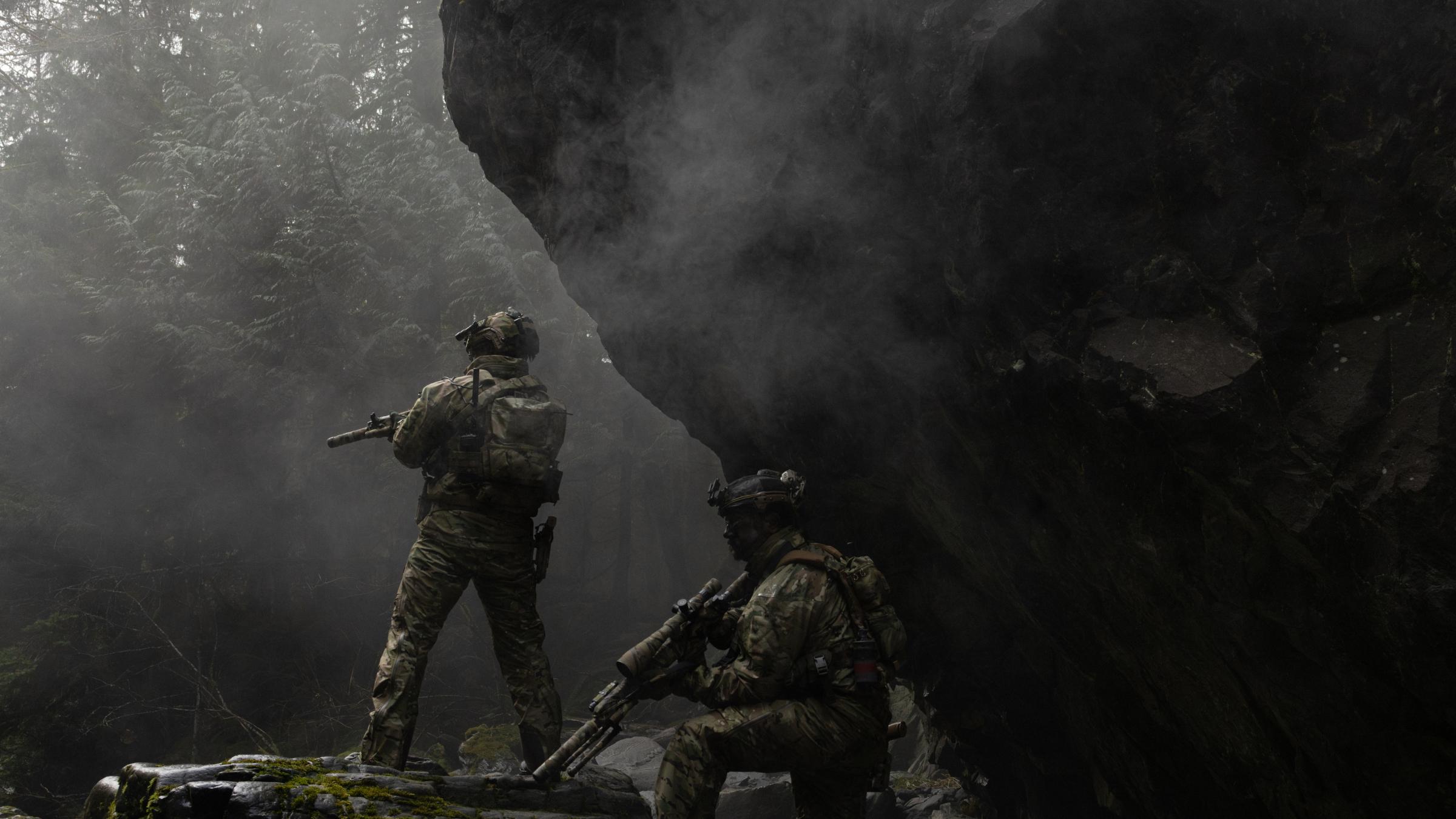 Two armed soldiers in tactical gear in a misty, rugged landscape.