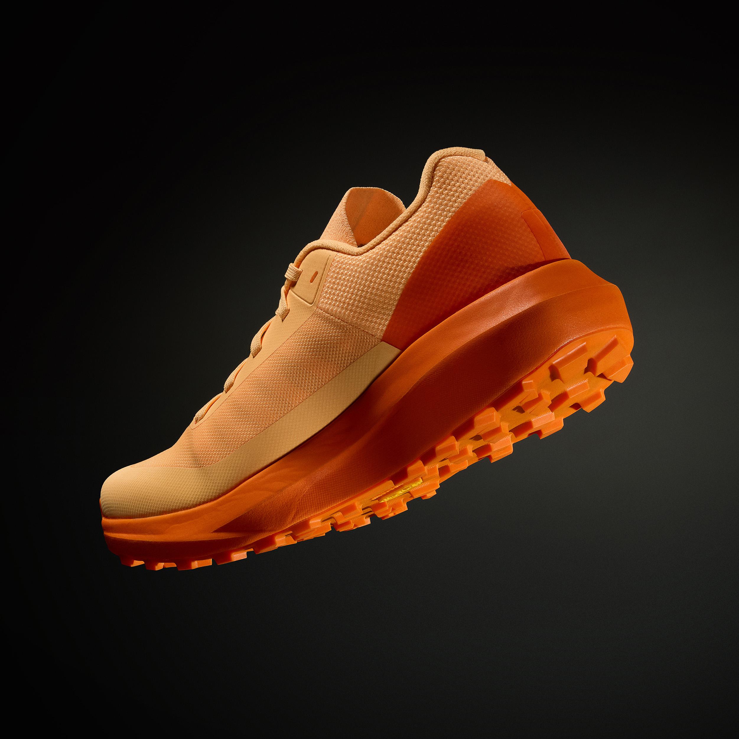a close up of a pair of orange running shoes on a black background .