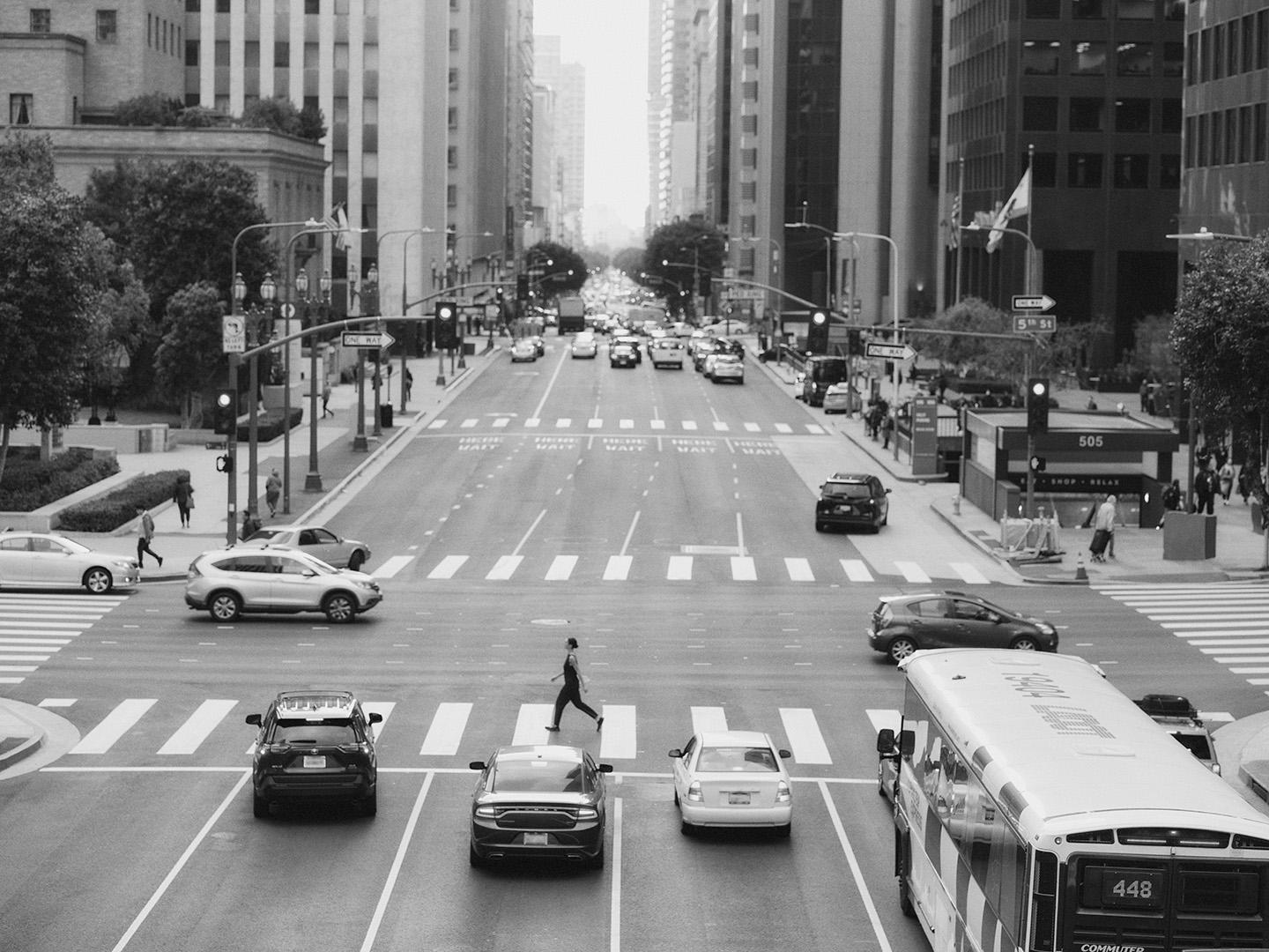 a black and white photo of a busy intersection in a city with a lady crossing the road