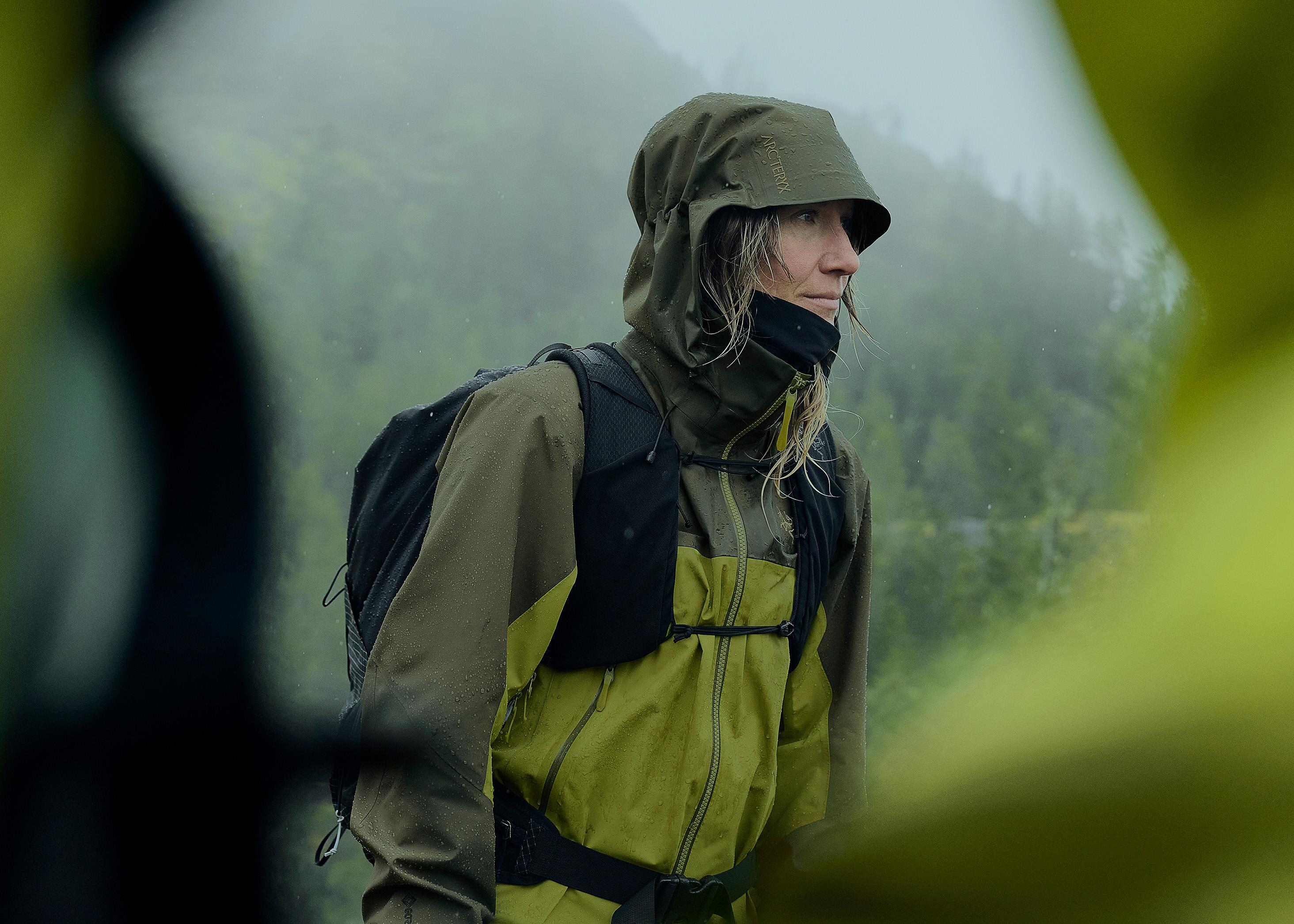 a woman wearing a green jacket and a backpack is standing in the rain .