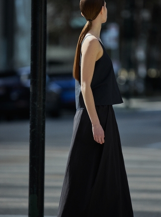 Woman in profile with a long ponytail, wearing a dark sleeveless top and long skirt outdoors.