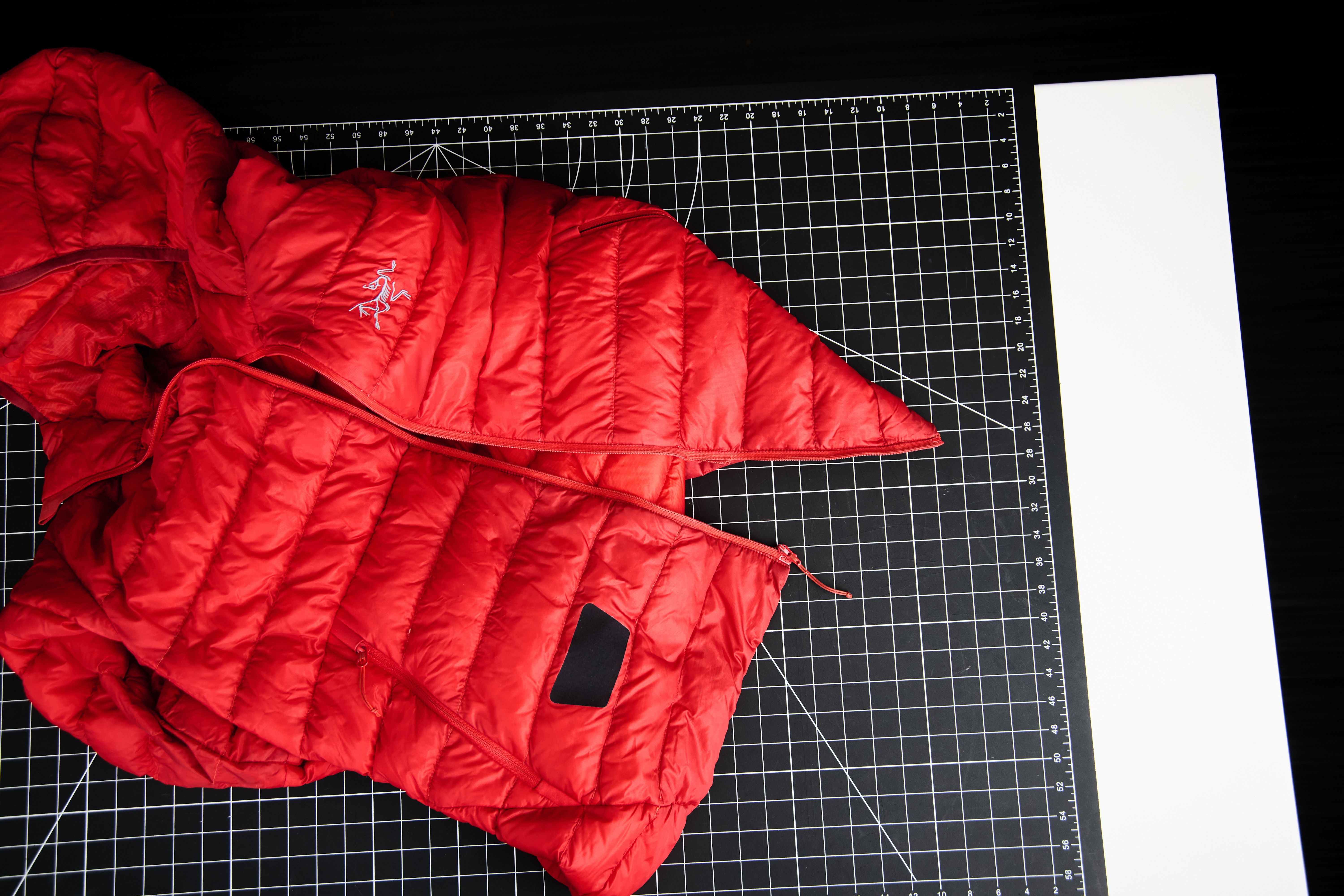 A red Arc'teryx puffer jacket on a black grid mat next to a white strip.