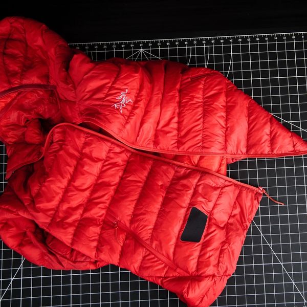 A red Arc'teryx puffer jacket on a black grid mat next to a white strip.