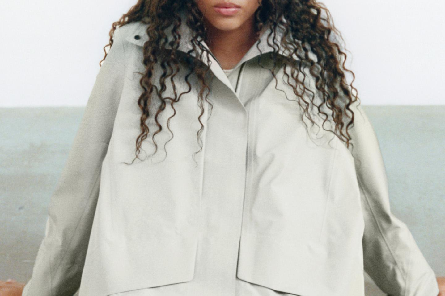 a woman with curly hair is wearing a white rain shell jacket