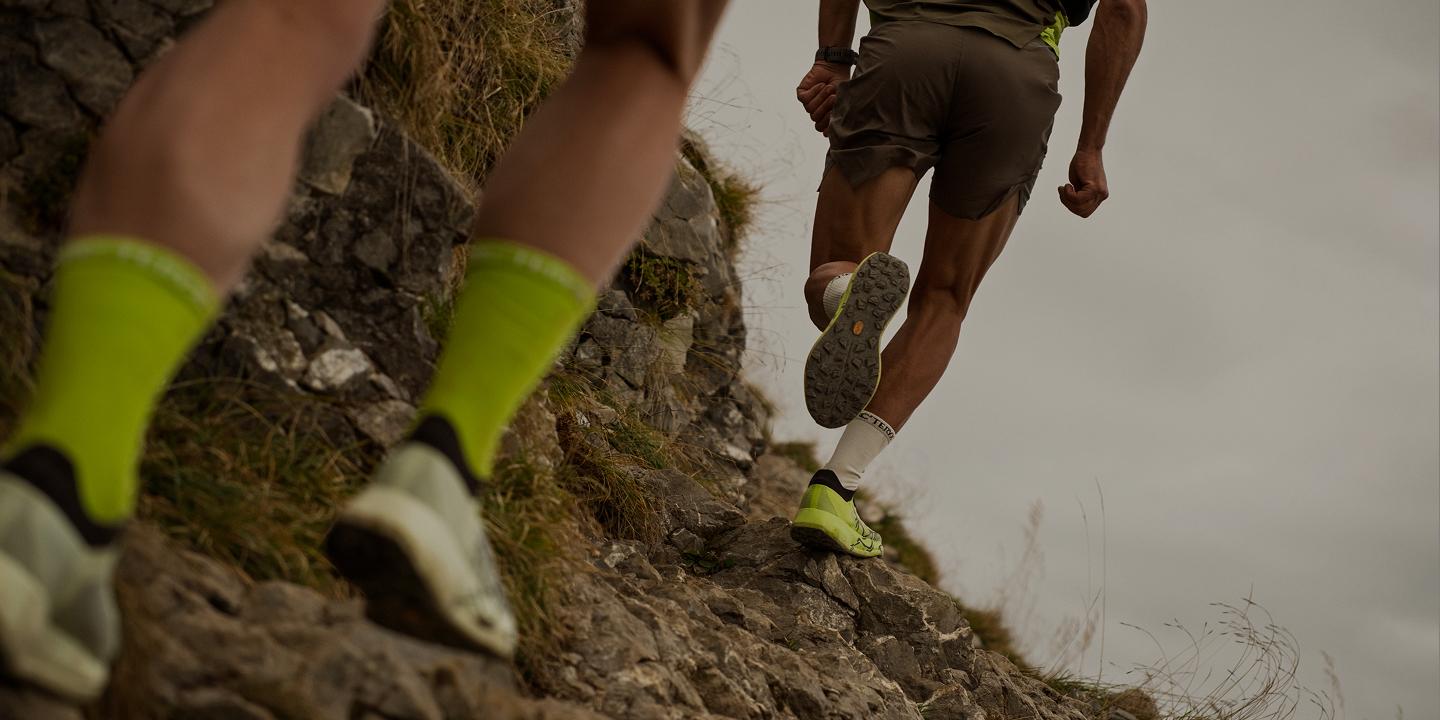 Two trail runners ascending a rocky path.