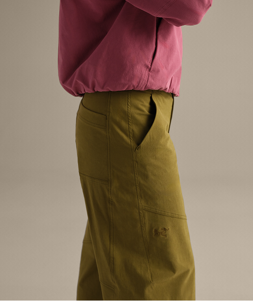 A person wears a pink top and olive green cargo pants with an embroidered logo.