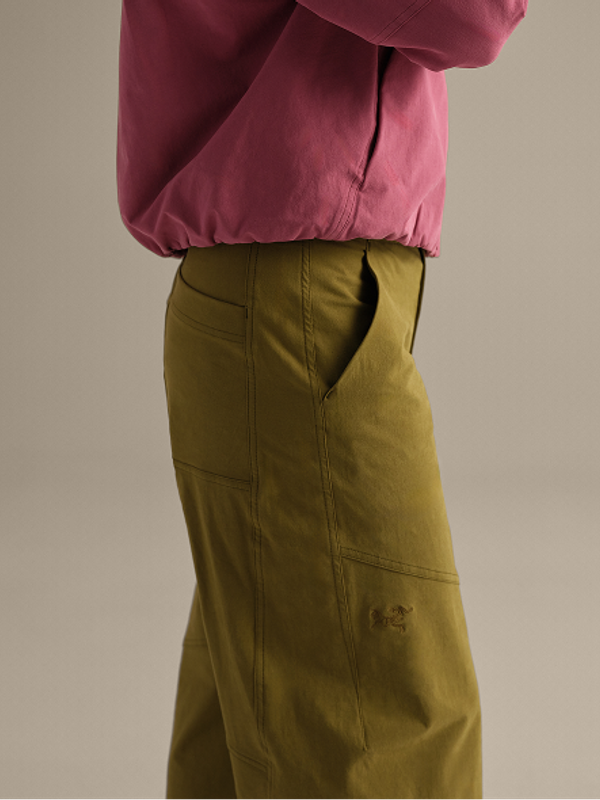 A person wears a pink top and olive green cargo pants with an embroidered logo.