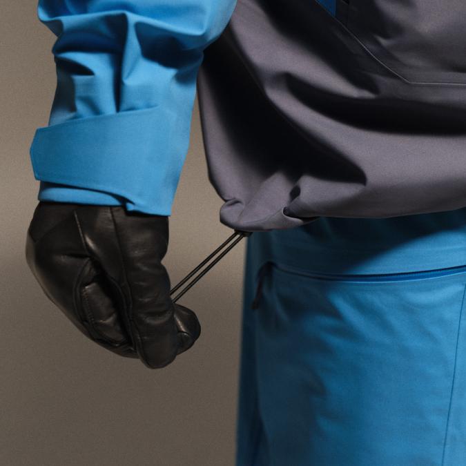 Gloved hand adjusting the drawcord of a blue and grey jacket.