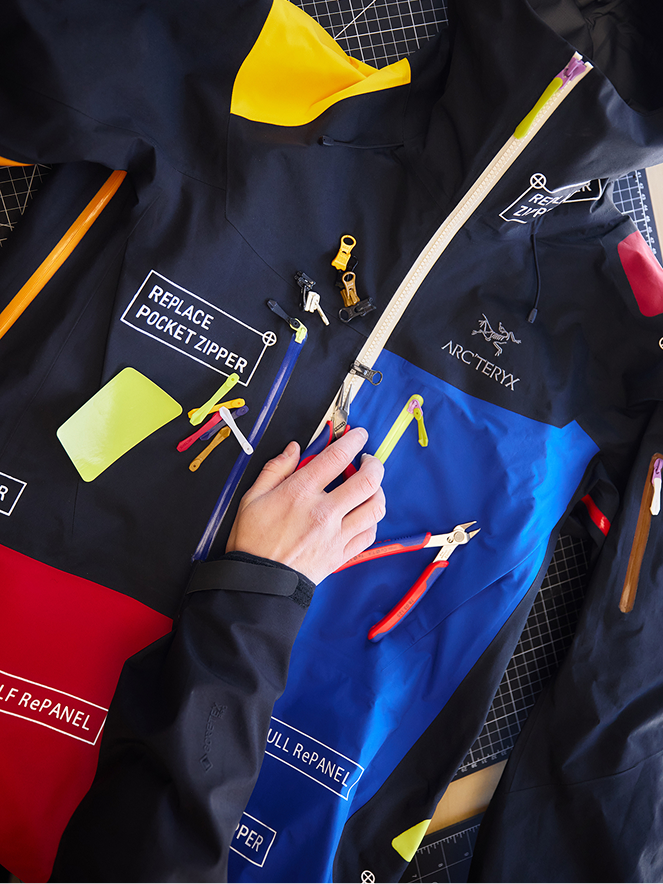 Hand repairing a multi-colored Arc'teryx jacket with tools and spare zipper parts.