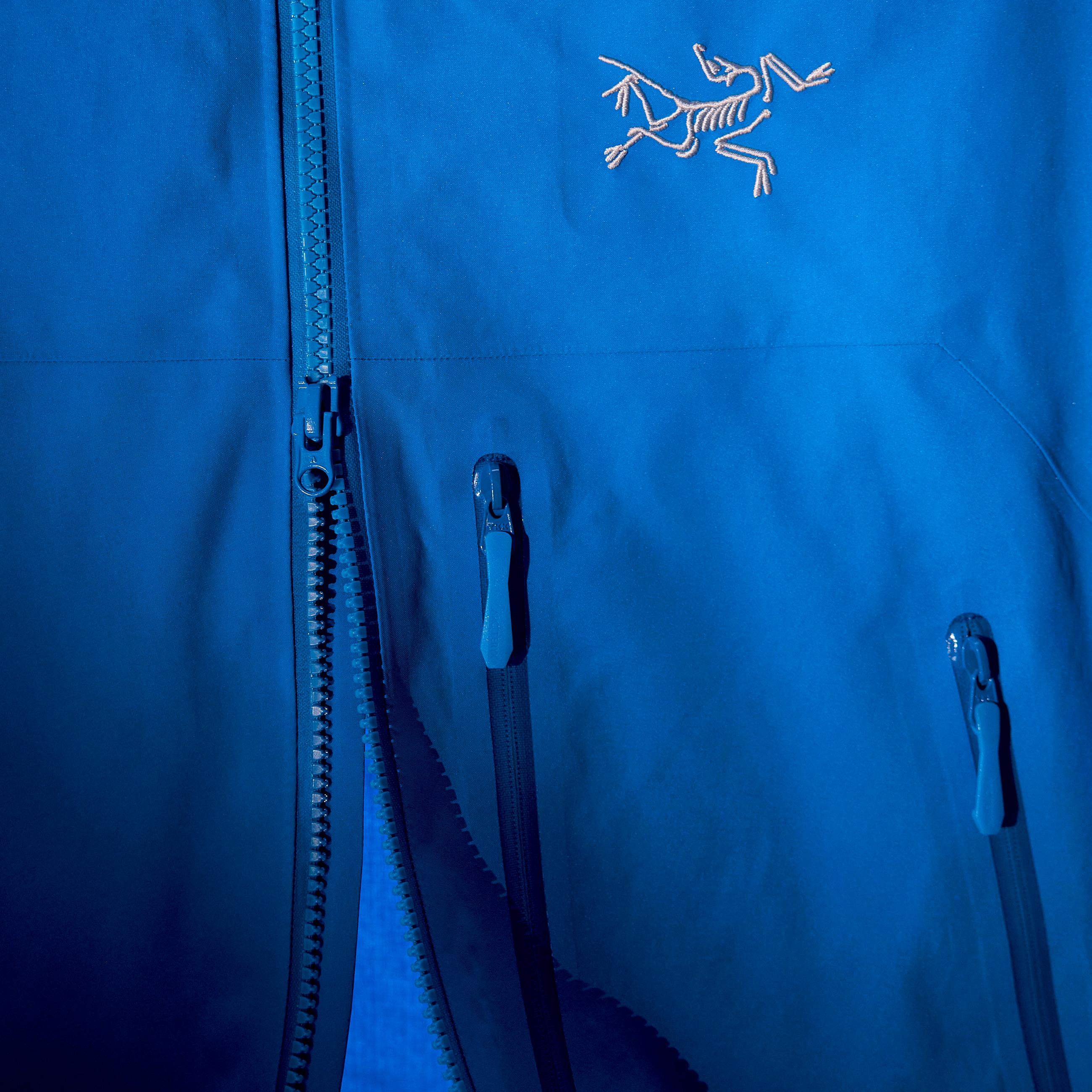 Bright blue Arc'teryx jacket with partially unzipped main zipper and two pocket zippers.