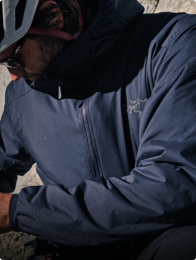 A person wearing a dark blue Arc'teryx jacket, helmet, and sunglasses.