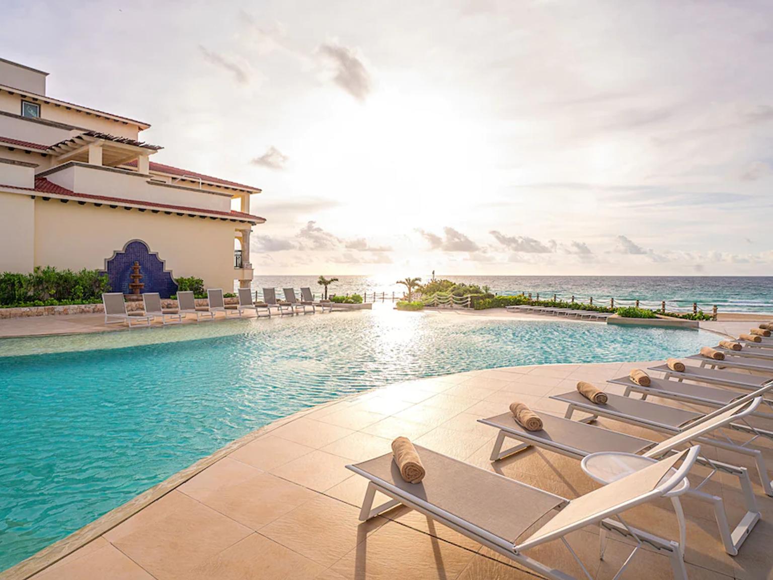 en stor simbassäng omgiven av solstolar och en byggnad bredvid havet