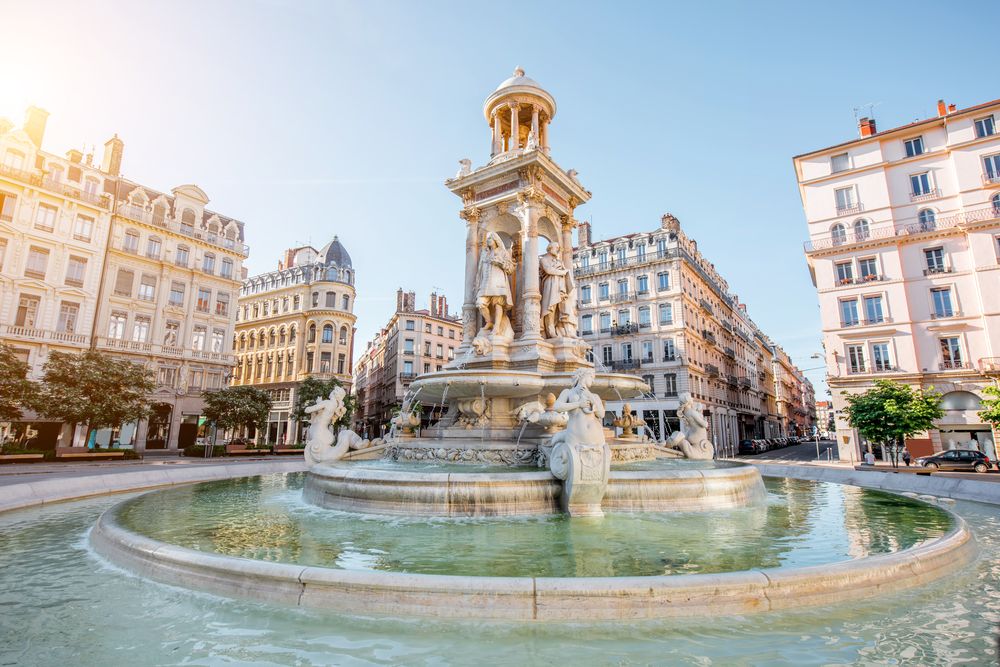 Place des Jacobins-fontænen i Lyon, Frankrig, omgivet af klassiske europæiske bygninger på en solrig dag.