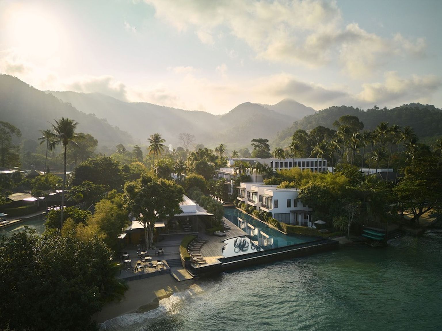 en luftfoto af et feriested omgivet af bjerge og træer ved siden af havet