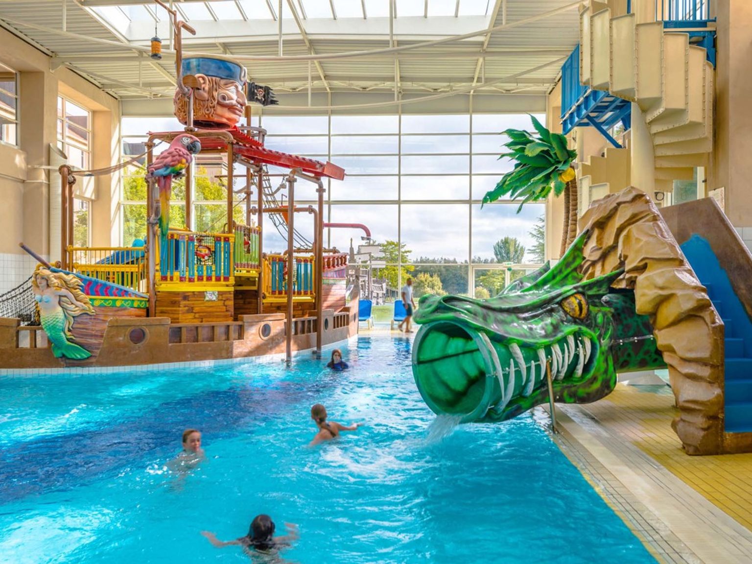 Inomhusvattenpark med en piratskeppslekstruktur, en drakrutschbana och barn som simmar. Explorers Hotel på Disneyland® Paris