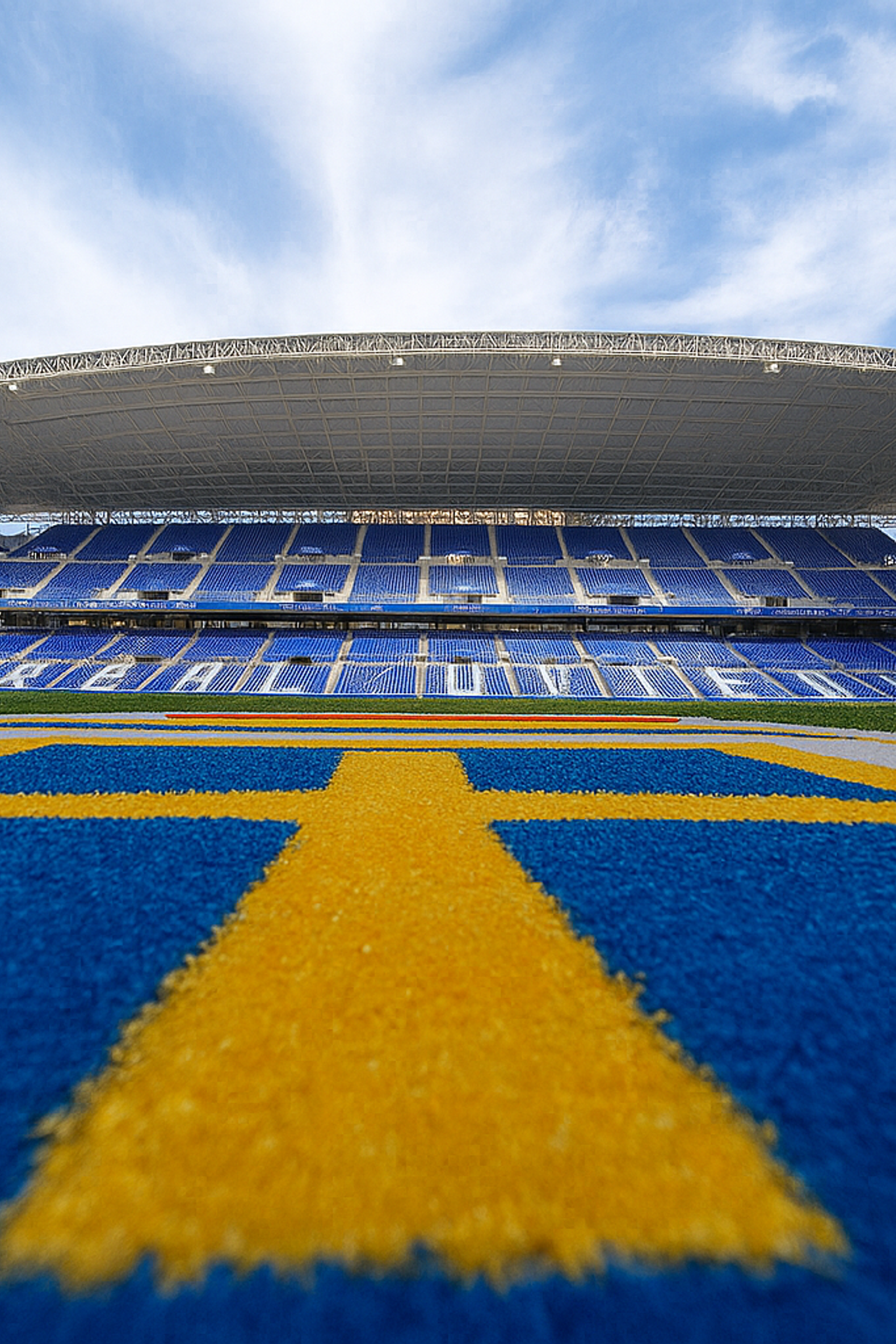 Leeres modernes Stadion mit blauen Sitzen, einem grünen Spielfeld und einer blauen Laufbahn mit gelben Markierungen.