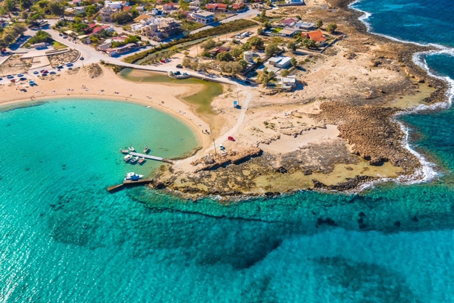 Luftfoto af en kystby med turkisblåt vand, sandstrande, klippefyldte kyster og både, der ligger fortøjet i en bugt.