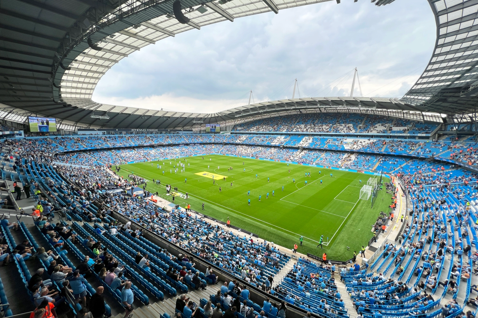 Fotbollsmatch på Etihad Stadium, med spelare på planen och fans på de blåa sätena.