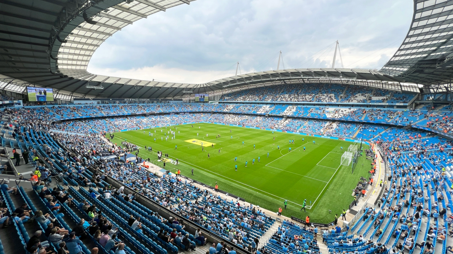 Fotbollsmatch på Etihad Stadium, med spelare på planen och fans på de blåa sätena.