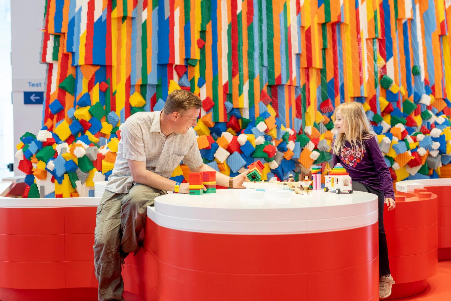 en man och en liten flicka sitter vid ett bord och leker med lego klossar