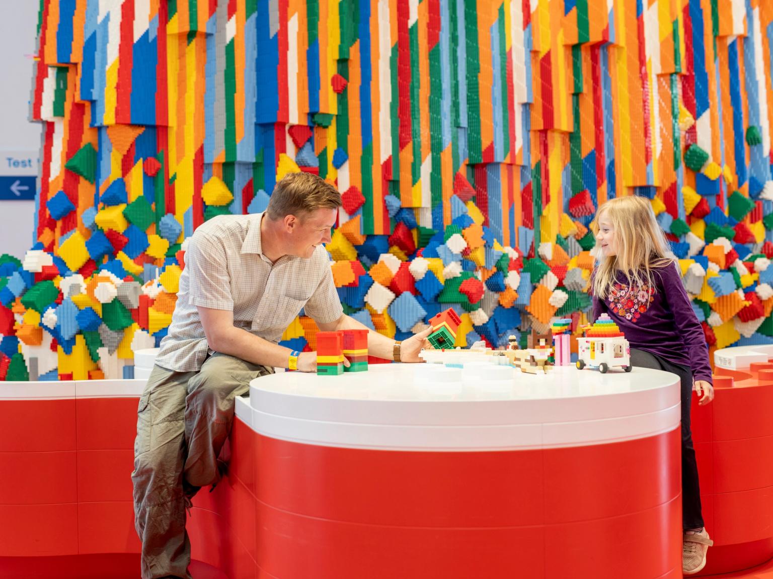 en man och en liten flicka sitter vid ett bord och leker med lego klossar