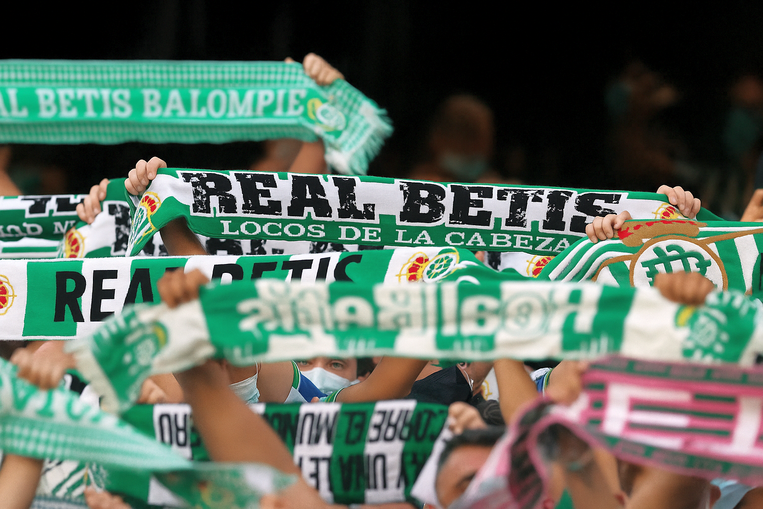 Football fans holding up green and white Real Betis scarves.