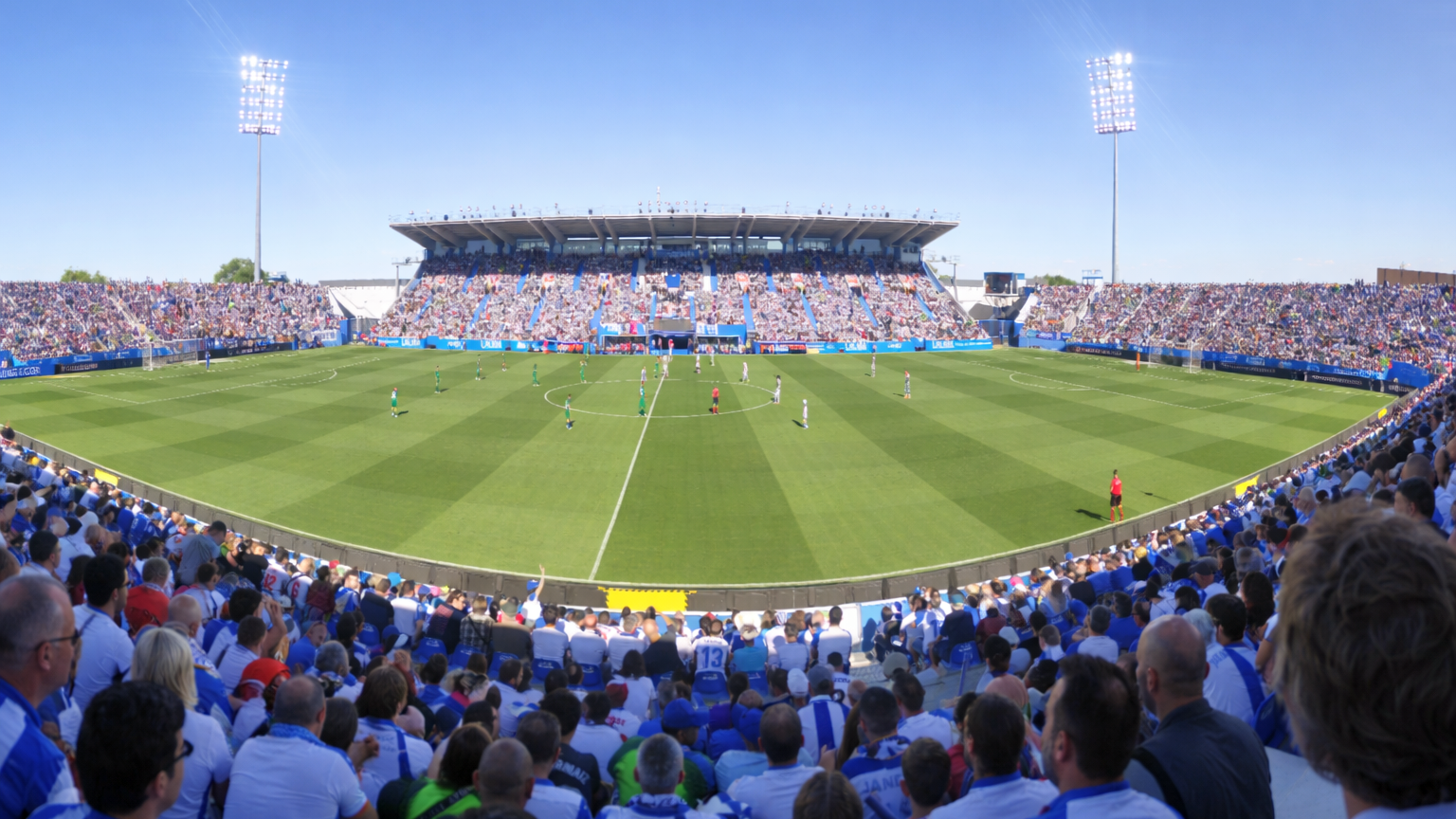 Vol voetbalstadion tijdens een dagwedstrijd, gezien vanaf de tribunes.