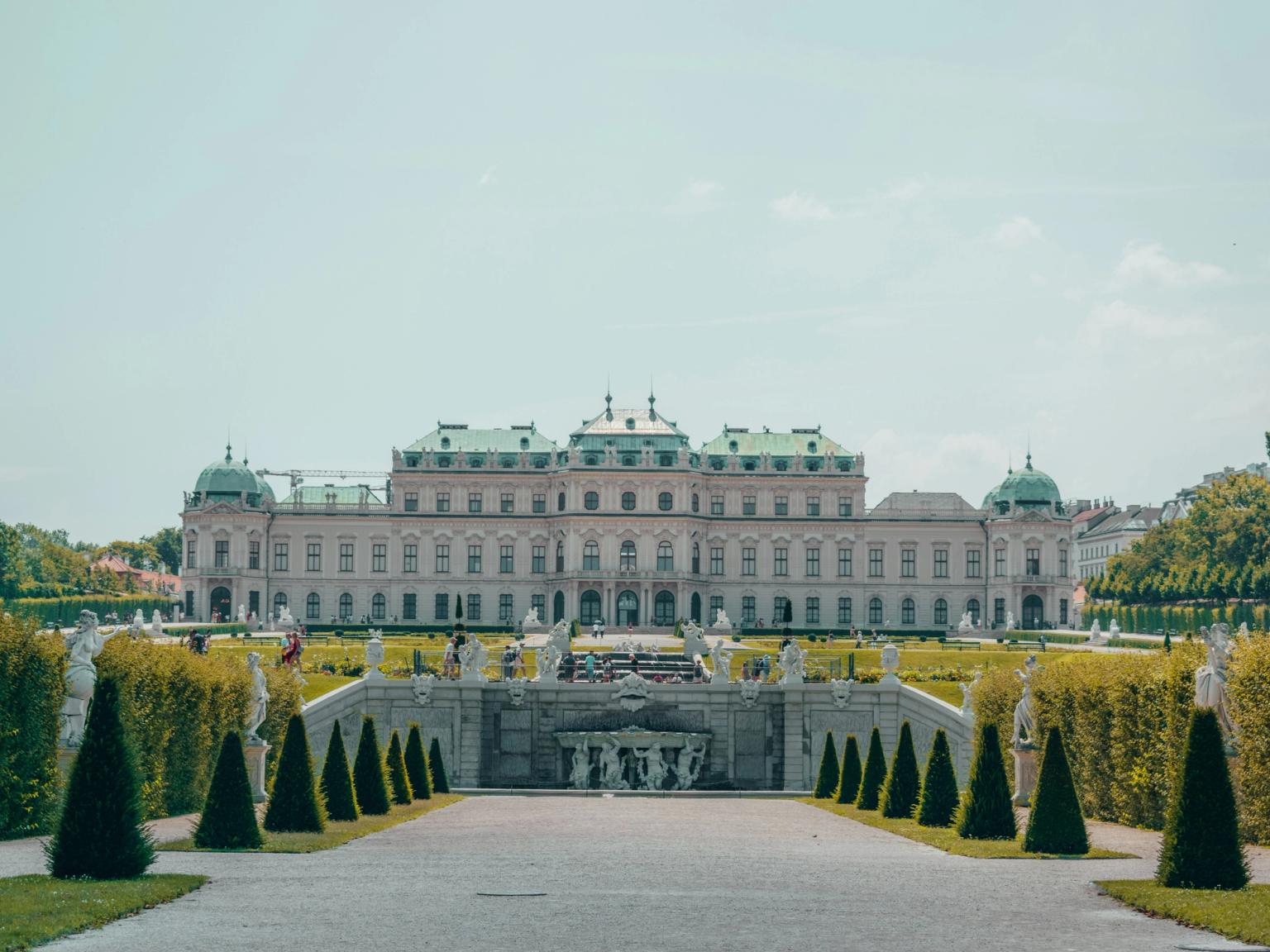 Belvederepalatset i Wien, en stor byggnad med en fontän framför, omgiven av träd och statyer.