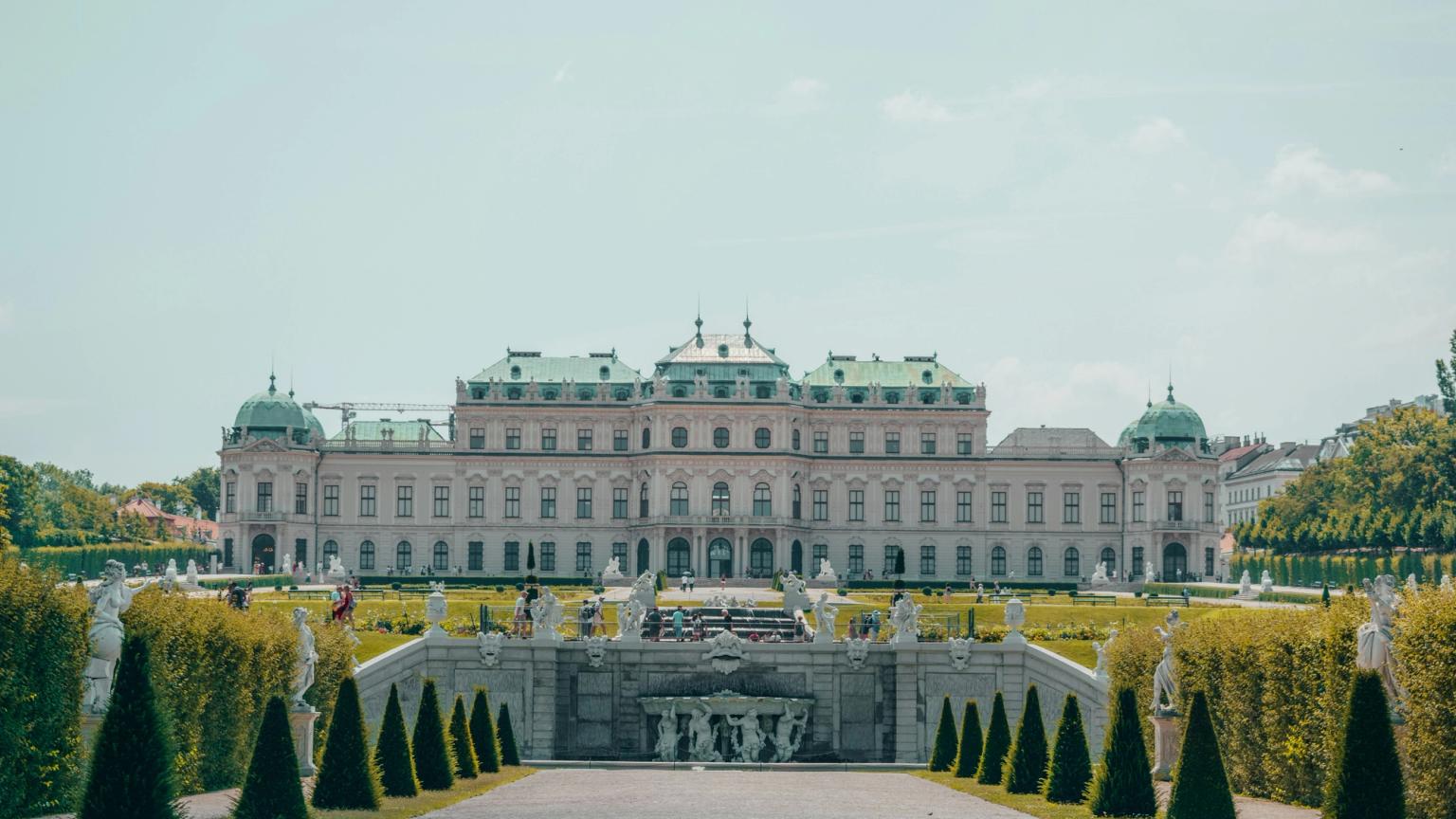 Belvederepalatset i Wien, en stor byggnad med en fontän framför, omgiven av träd och statyer.