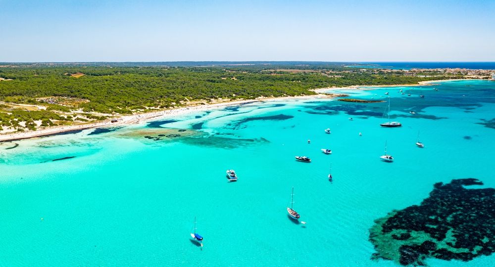 Luftfoto af en tropisk bugt med turkis vand, en sandstrand og flere både. Es Trenc, Mallorca