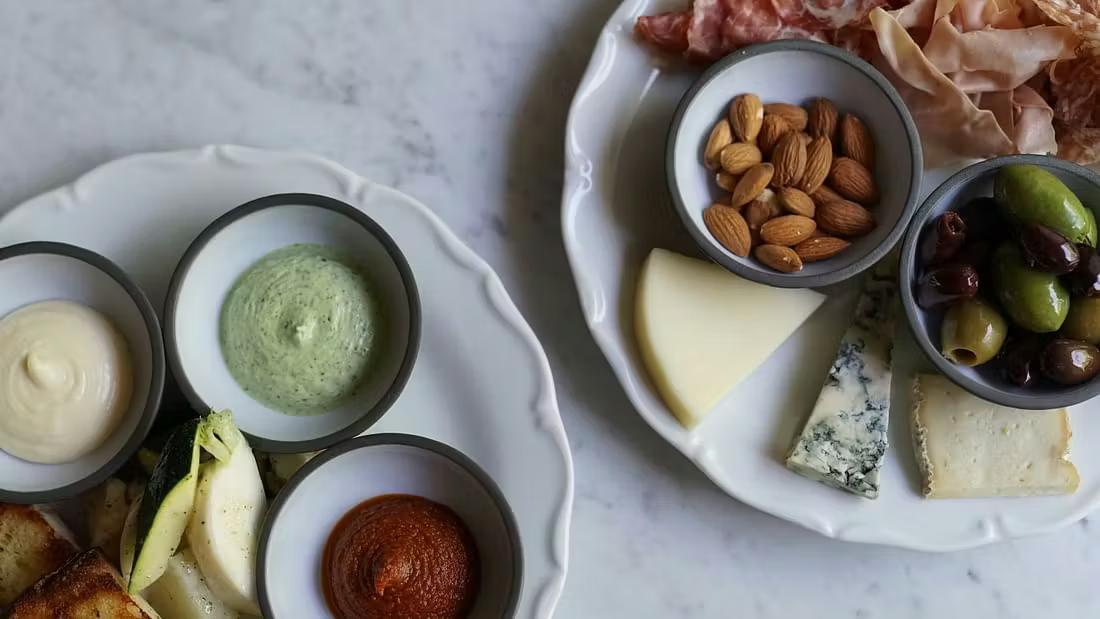 To charcuteribrætter med oste, kureret kød, dips, oliven, mandler og brød.