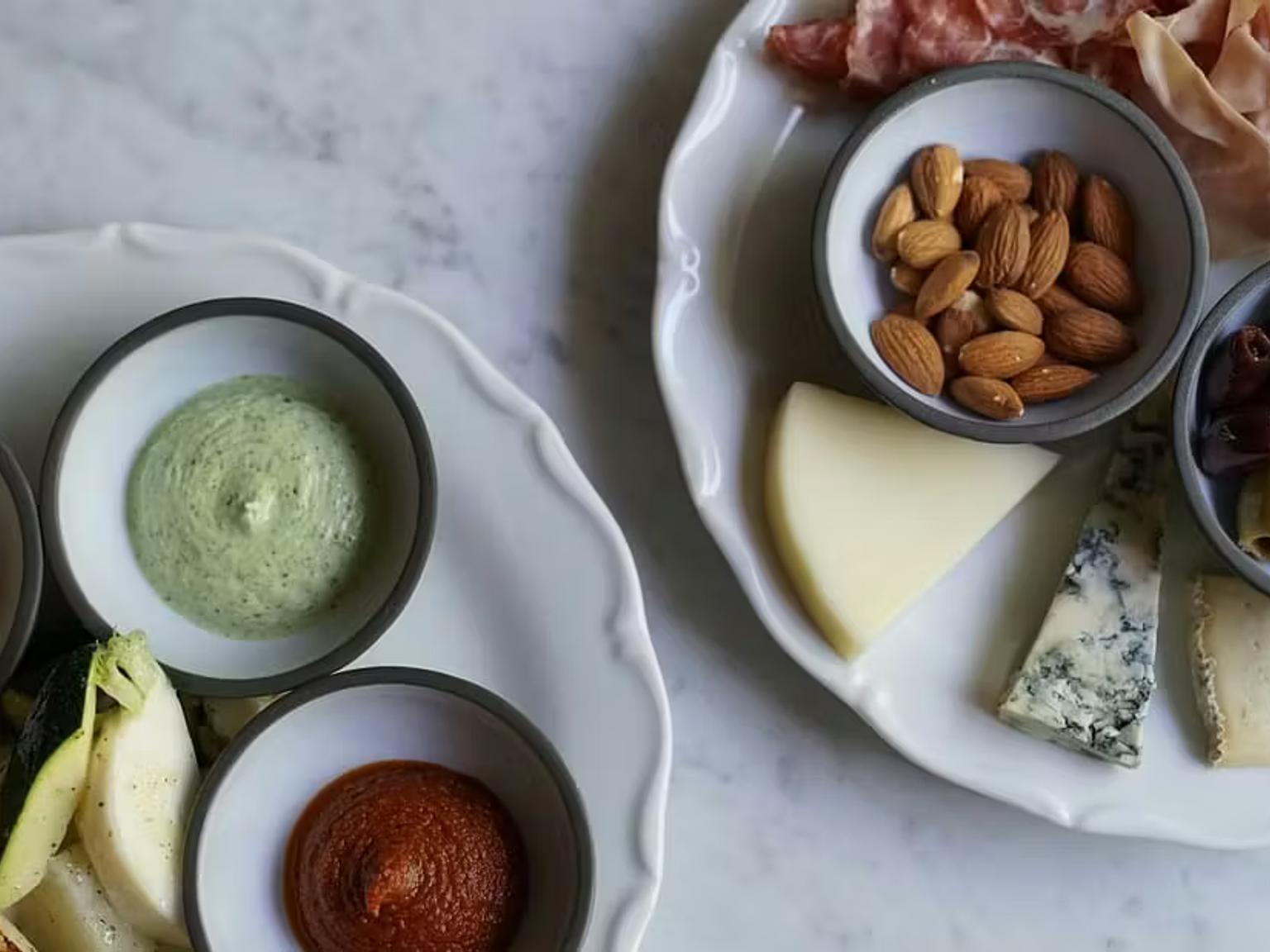 To charcuteribrætter med oste, kureret kød, dips, oliven, mandler og brød.