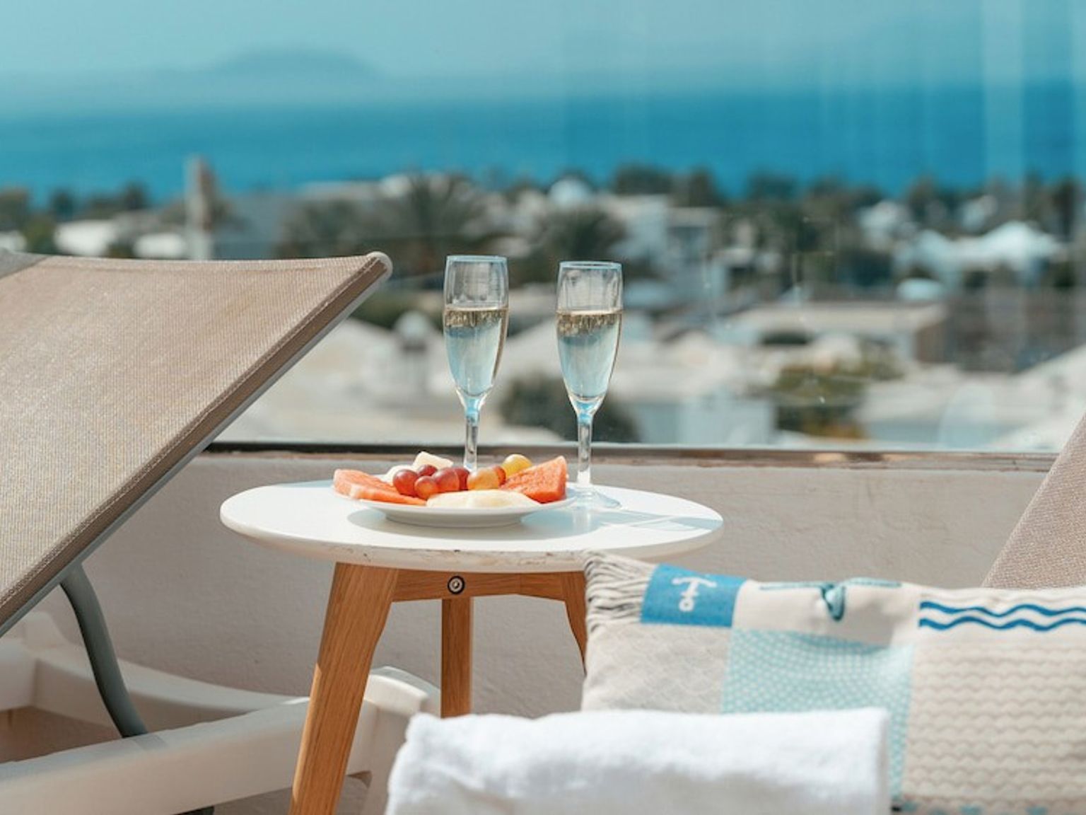 Balkong med solsenger, to glass champagne, en frukttallerken og havutsikt.
