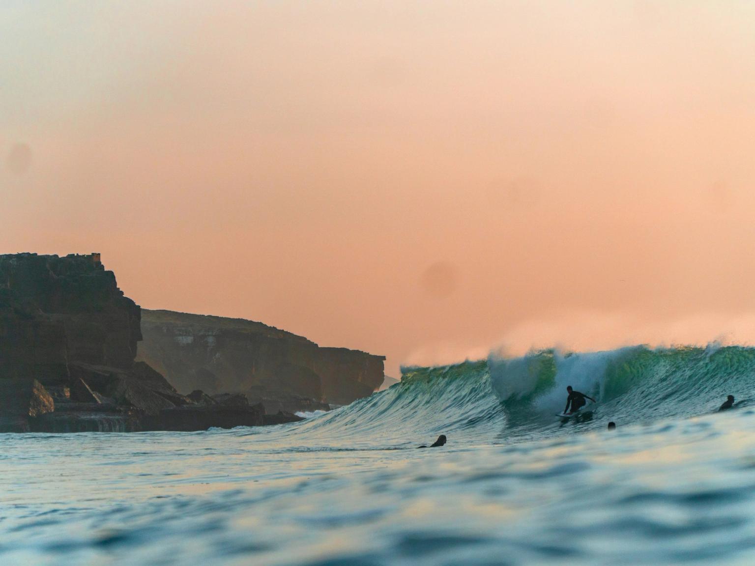 a group of surfers are riding a wave in the ocean at sunset.