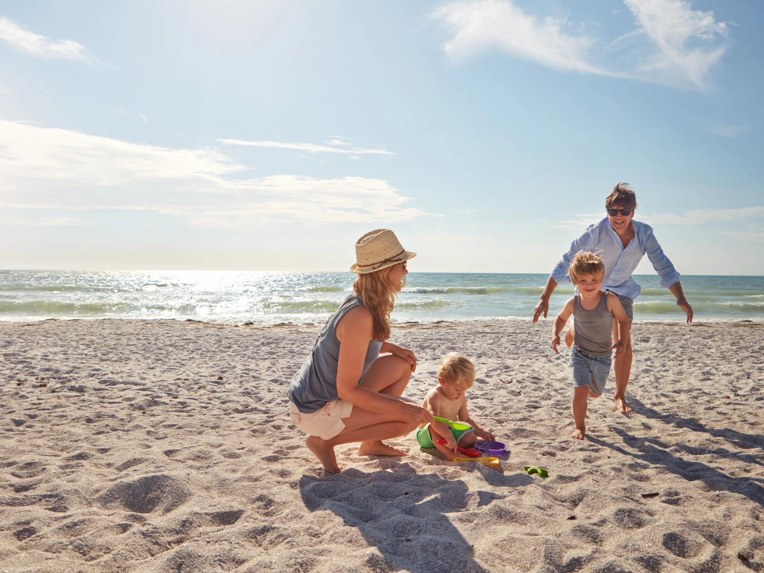 En familj med två små barn som leker på en solig strand.