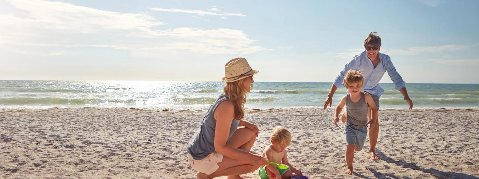 En familj med två små barn som leker på en solig strand.