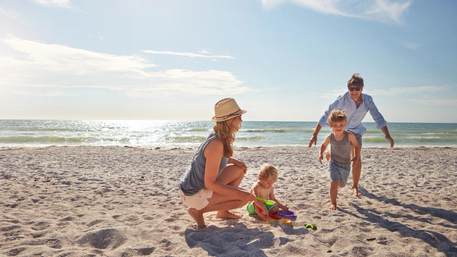 En familj med två små barn som leker på en solig strand.