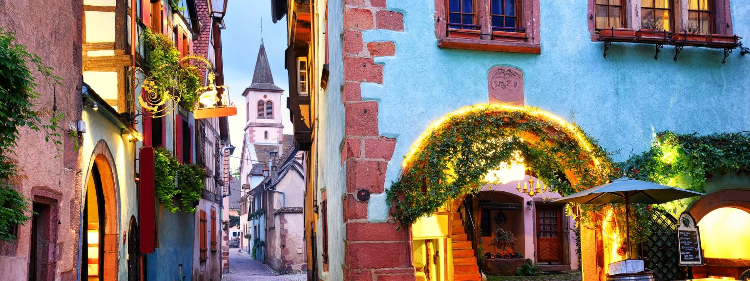 en smal brosteinsgate i en liten by med en kirke i bakgrunnen